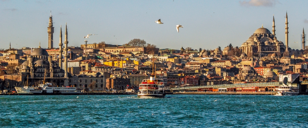 Vista dell'orizzonte di Istanbul al tramonto, con l'iconica Torre di Galata che spicca su un fitto panorama urbano fatto di edifici storici e imbarcazioni che solcano le acque del Corno d'Oro.